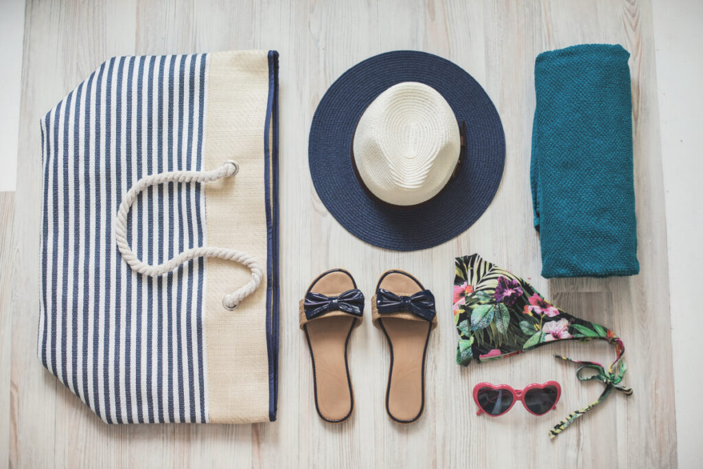 Beach bag, female slippers, sun hat, beach towel, bikini, and sunglasses are arranged on table