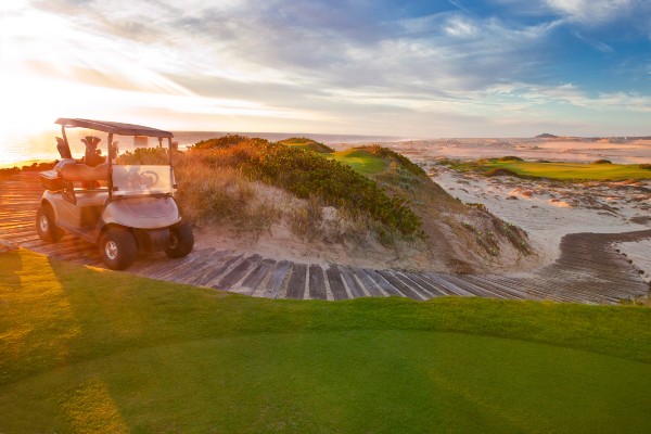 A golf cart on a path with a view of the clear blue sky and the beach in the distance offers a scenic and relaxing atmosphere