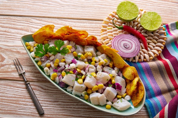 A vibrant plate of ceviche with fresh fish marinated in citrus, garnished with cilantro, red onions, and yellow corn, served alongside crispy tortilla chips.