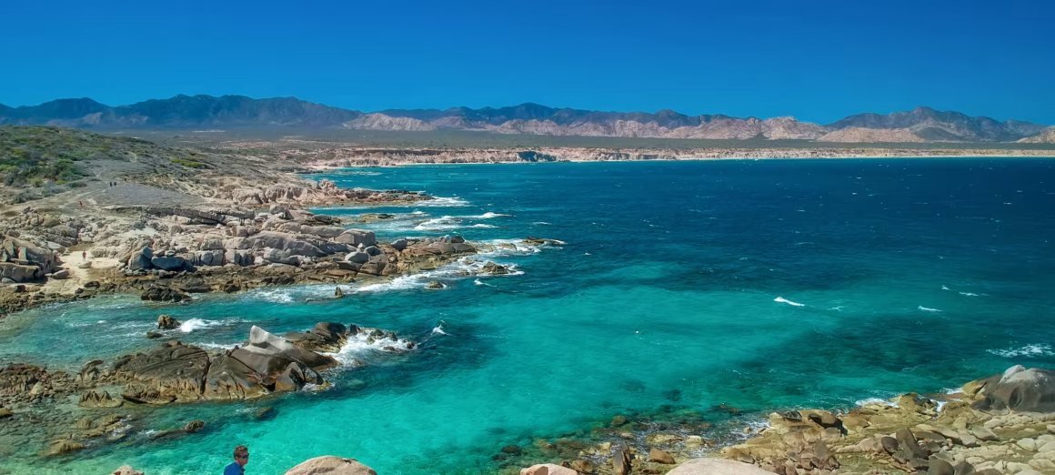 Aerial view of East Cape beach, showcasing the serene coastline with crystal-clear waters, white sandy beaches, and rugged hills in the background