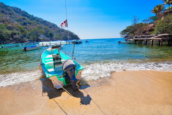 A boat rests on the sandy shore, and crystal-clear turquoise waters gently lap the beach, creating a peaceful and idyllic coastal scene.