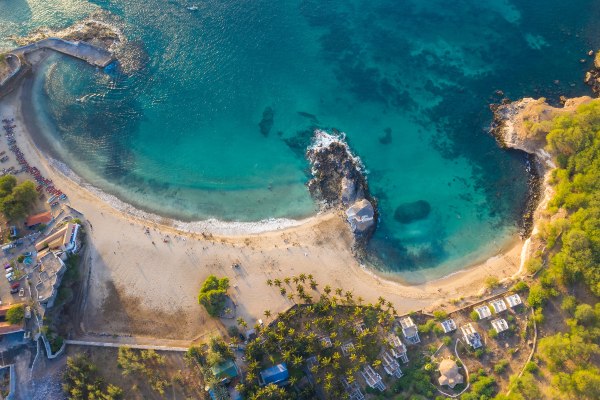 Aerial view of East Cape's beach showcasing the golden sand, clear turquoise water, and surrounding cliffs under a bright blue sky