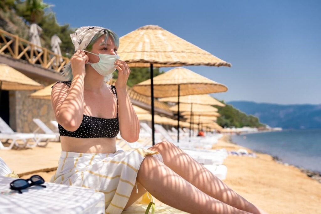 alt="young woman wearing mask while sunbathing on the beach"